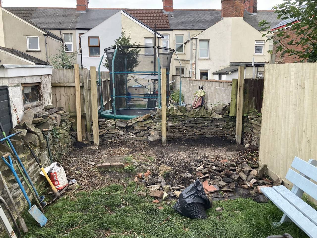 New timber fence posts set in the ground in front of an old stone wall